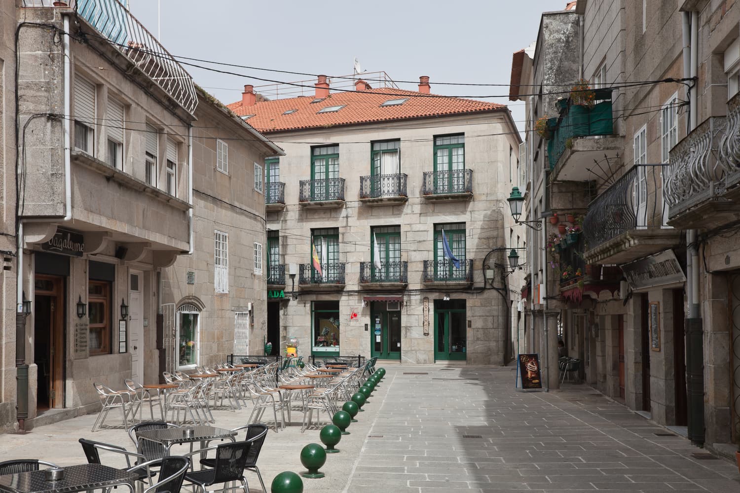 Stone houses with balconies and café terraces on a small square in Baiona’s old town