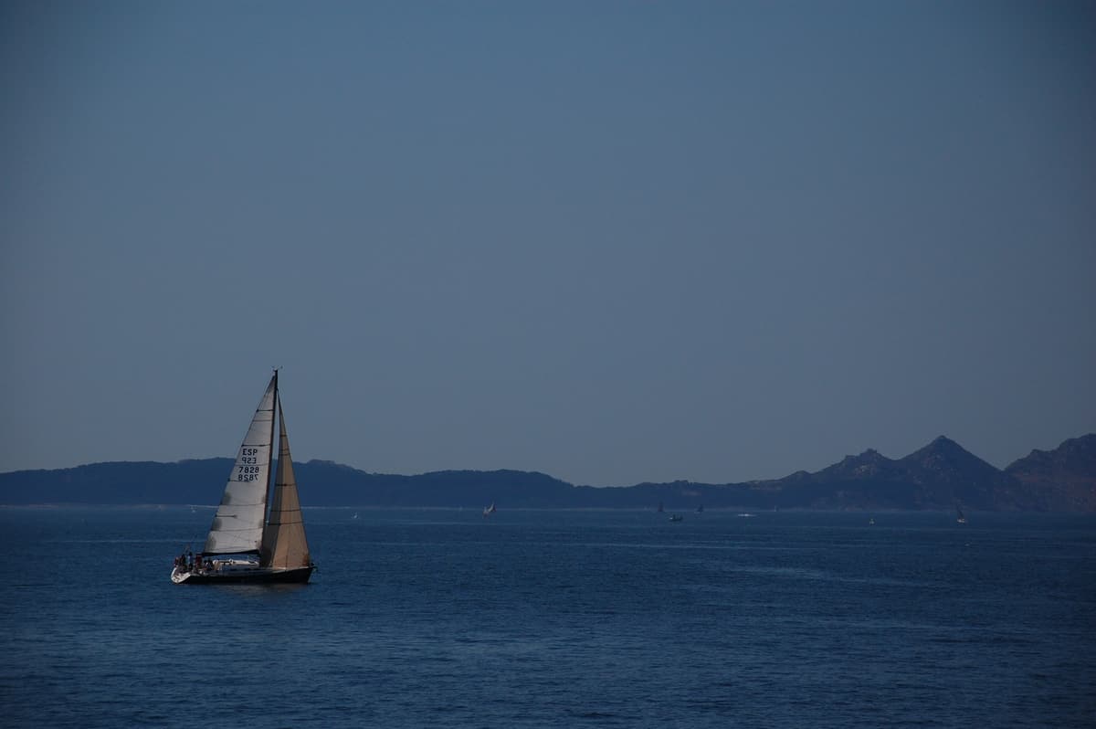 A sailing yacht crossing the Ría de Vigo with the Cíes Islands on the horizon